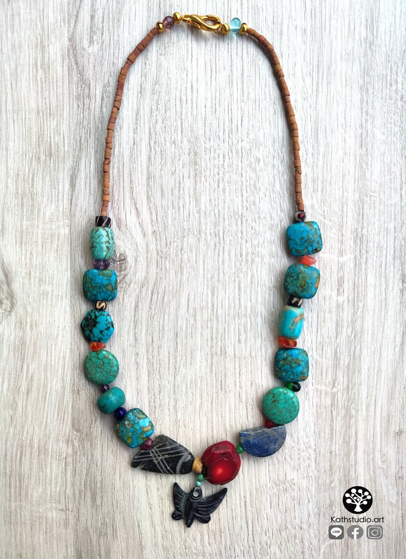 Peut inclure: Un collier de perles turquoise, rouge et noir avec un pendentif en forme de papillon. Le collier est fait de pierres naturelles et a un fermoir en or.