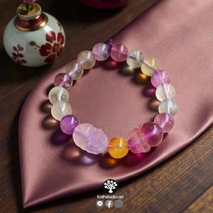 May include: A beaded bracelet featuring translucent, multi-colored fluorite spheres in shades of purple, yellow, and pale green. The bracelet includes two carved skull-shaped beads and one smooth yellow bead, all strung on a purple cord.