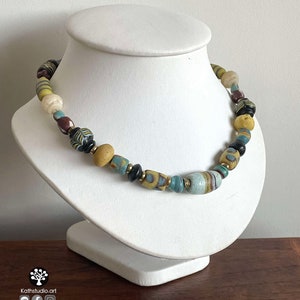 May include: A necklace made of colorful glass beads in shades of blue, yellow, brown, and black. The beads are of various shapes and sizes, and some have intricate patterns.