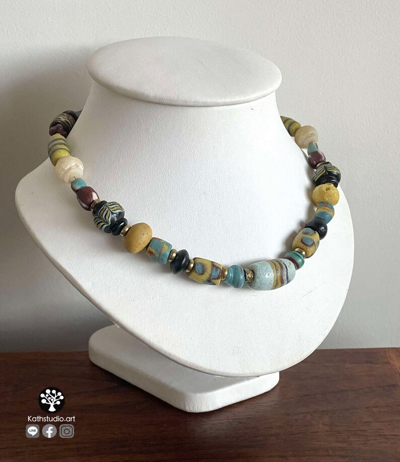 May include: A necklace made of colorful glass beads in shades of blue, yellow, brown, and black. The beads are of various shapes and sizes, and some have intricate patterns.