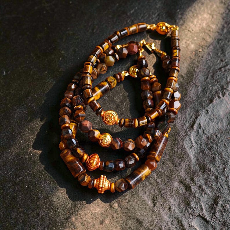 May include: A collection of four bracelets crafted from faceted tiger eye beads in shades of brown and gold. Each bracelet features a central gold-toned metal spacer bead with intricate embossed patterns and a gold-toned metal clasp closure.