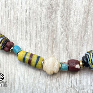 May include: A close-up of a colorful beaded necklace with a variety of shapes and sizes. The beads are made of glass and have a variety of colors, including yellow, blue, red, and black. The necklace is on a wooden surface.