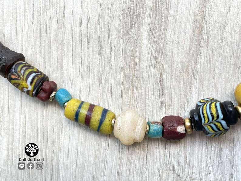 May include: A close-up of a colorful beaded necklace with a variety of shapes and sizes. The beads are made of glass and have a variety of colors, including yellow, blue, red, and black. The necklace is on a wooden surface.