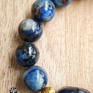 Pu&ograve; includere: Un bracciale composto da perle sferiche levigate di cianite blu con visibili inclusioni scure e una singola perlina distanziatrice color oro metallizzato. Le perle sono infilate insieme, mostrando una superficie liscia e lucida in toni blu.