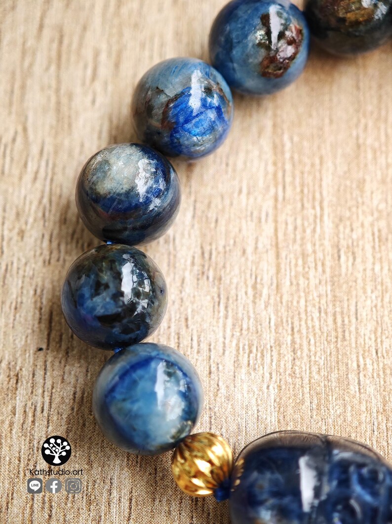 Pu&ograve; includere: Un bracciale composto da perle sferiche levigate di cianite blu con visibili inclusioni scure e una singola perlina distanziatrice color oro metallizzato. Le perle sono infilate insieme, mostrando una superficie liscia e lucida in toni blu.