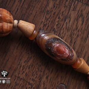 May include: Close-up of a wooden beaded necklace with a carved, textured bead and a central oval bead with a red center. The beads are various shades of brown and orange.