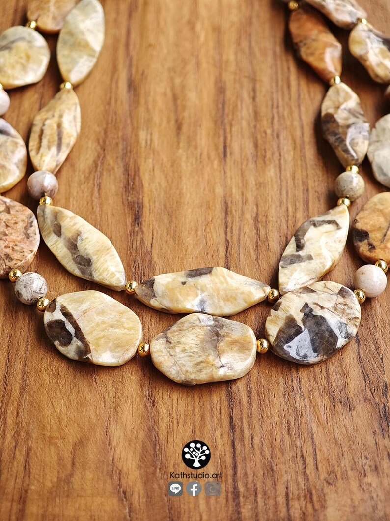 Puede incluir: Un collar de varias hileras con cuentas de piedra pulidas e irregulares en tonos beige y marr&oacute;n, intercaladas con peque&ntilde;as cuentas espaciadoras redondas de color dorado met&aacute;lico. El collar presenta un dise&ntilde;o en capas con formas variadas.