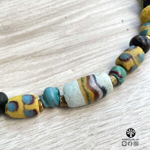 May include: A close-up of a necklace made of colorful glass beads. The beads are a mix of yellow, blue, green, and white. Some of the beads have a striped pattern. The necklace is on a wooden surface.