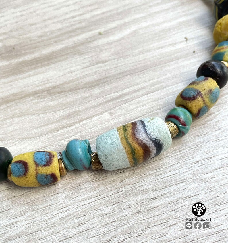 May include: A close-up of a necklace made of colorful glass beads. The beads are a mix of yellow, blue, green, and white. Some of the beads have a striped pattern. The necklace is on a wooden surface.