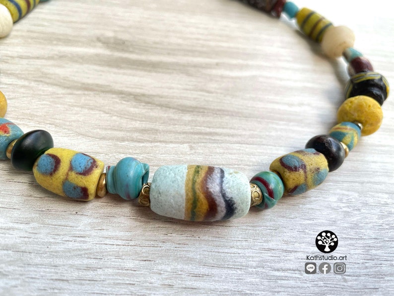 May include: A colorful necklace made of various glass beads, including yellow, blue, green, and brown. The beads are strung together on a cord and have a variety of patterns and textures.