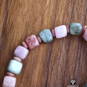 May include: A beaded bracelet featuring alternating square-shaped beads in shades of pale pink, dusty rose, and sage green, separated by small, rounded, light pink spacer beads. The text Kathstudio.art is printed in the bottom right corner.