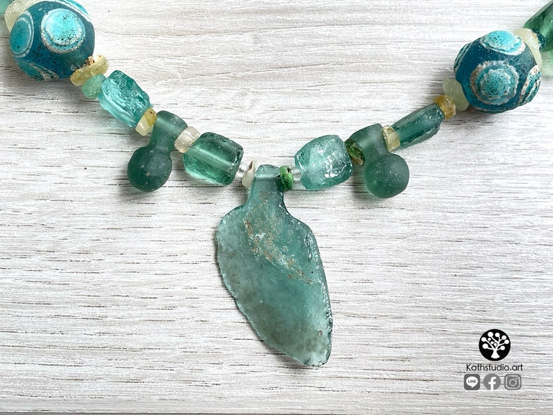 Puede incluir: Collar artesanal con cuentas de vidrio marino en tonos turquesa y transparente. El collar incluye un colgante central con forma de botella. Las cuentas est&aacute;n ensartadas en un cord&oacute;n verde, creando un accesorio &uacute;nico.