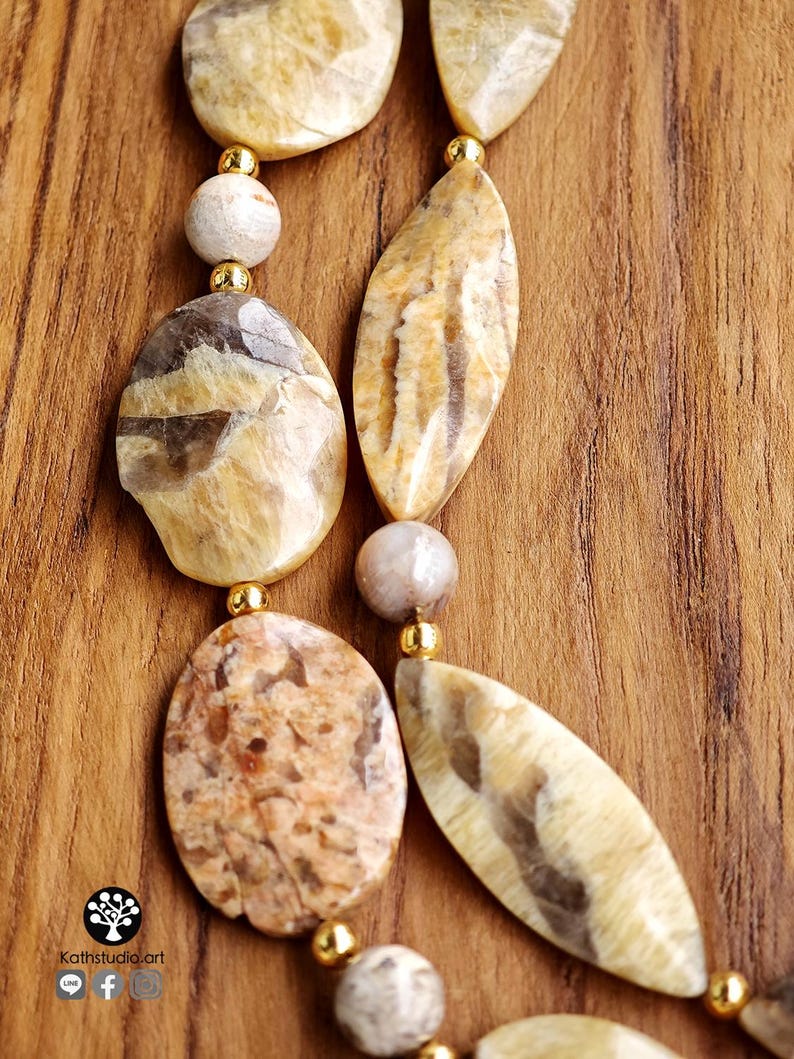 Puede incluir: Un collar con piedras pulidas de diversas formas en tonos beige, marr&oacute;n y ocre, intercaladas con peque&ntilde;as cuentas redondas de metal color oro. Las piedras presentan vetas naturales y texturas variadas dispuestas en un patr&oacute;n lineal.