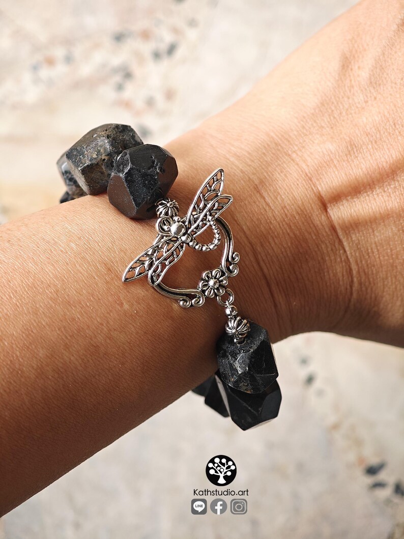 May include: A bracelet composed of large, faceted, matte black beads strung together. The piece features a prominent silver-toned metal toggle clasp shaped like a dragonfly with intricate filigree wings and a small flower detail at the base.