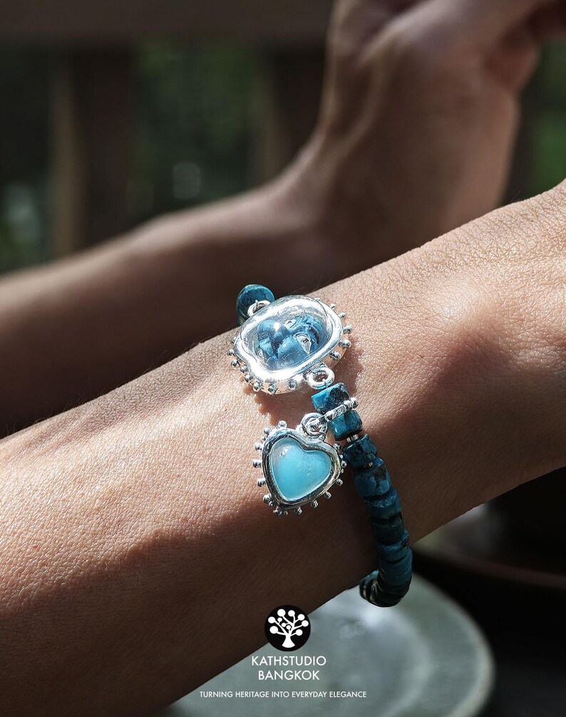 Puede incluir: Una pulsera con cuentas de piedra texturizadas de color azul oscuro y dos dijes plateados. Un dije es un engaste circular de borde festoneado con una piedra azul, y el otro es un engaste en forma de coraz&oacute;n con una piedra azul claro.