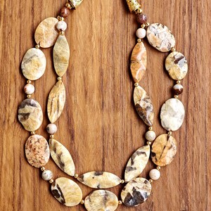 Puede incluir: Un collar de dos hilos con piedras pulidas de color beige y marr&oacute;n con patrones, en formas ovaladas y de marquesa. El collar incluye peque&ntilde;as cuentas espaciadoras doradas y terminales c&oacute;nicos dorados con cierre de mosquet&oacute;n.