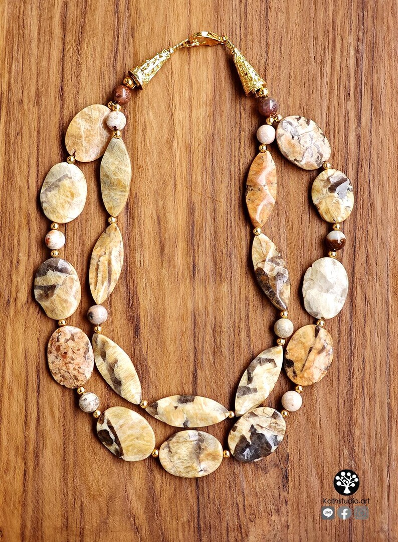 Puede incluir: Un collar de dos hilos con piedras pulidas de color beige y marr&oacute;n con patrones, en formas ovaladas y de marquesa. El collar incluye peque&ntilde;as cuentas espaciadoras doradas y terminales c&oacute;nicos dorados con cierre de mosquet&oacute;n.