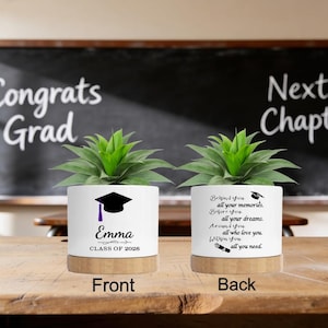 May include: Two white ceramic planters with green plants, each on a wooden base. One planter has a graduation cap graphic, the name "Emma", and "CLASS OF 2026". The other has a graduation quote. The background is a chalkboard.