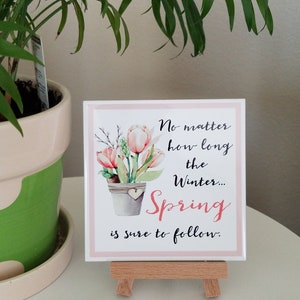 May include: A pink and white square tile with a watercolor illustration of a potted plant with pink flowers. The tile has the text "No matter how long the winter... Spring is sure to follow."