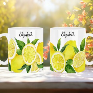 May include: Two white ceramic mugs with a lemon design. The mugs have the name "Elizabeth" printed on them.