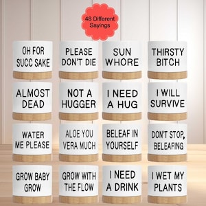 May include: A collection of white ceramic pots with various humorous phrases in black text, including "Oh for Succ Sake" and "I Wet My Plants." Each pot has a natural wood-colored base. A red, flower-shaped graphic reads "48 Different Sayings."