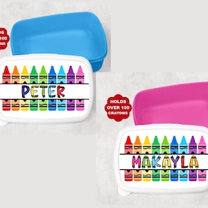 May include: Two personalized crayon boxes, one blue and one pink, each with a white lid. The lids feature a colorful crayon design and a name, "PETER" and "MAKAYLA". Each box holds over 100 crayons.
