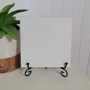 May include: A white ceramic tile with a black metal easel stand. The tile is blank and ready to be decorated.