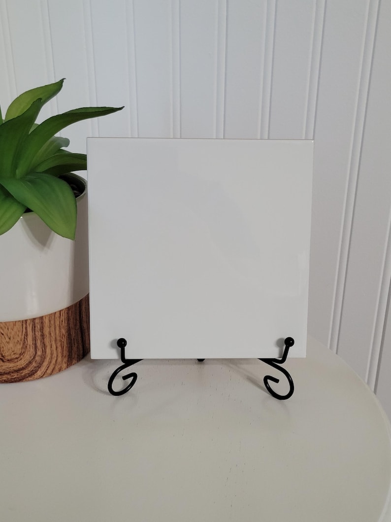 May include: A white ceramic tile with a black metal easel stand. The tile is blank and ready to be decorated.