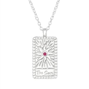 May include: Silver necklace with a rectangular pendant featuring a stylized sun design with a red gemstone in the center. The pendant has a border and the text "The Sun" inscribed on it.