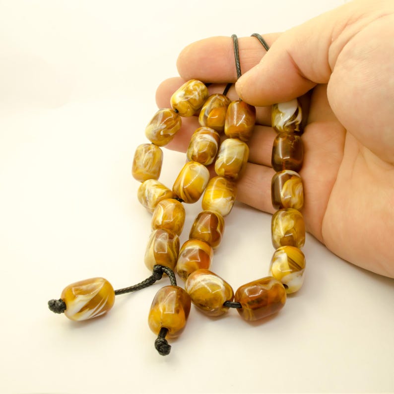 May include: A string of amber prayer beads with white swirls. The beads are strung on a black cord and have a tassel at the end.