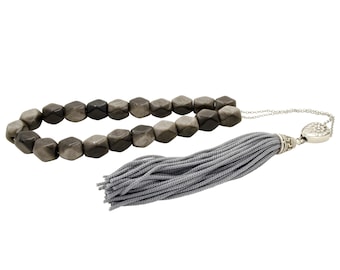 May include: A gray and black beaded prayer necklace with a silver tassel and a silver charm. The beads are faceted and have a geometric shape.