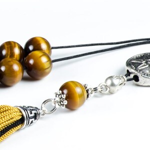 K&ouml;nnte beinhalten: Nahaufnahme einer Halskette mit Tigeraugenperlen. Die Halskette hat eine goldene Quaste und ein silberfarbenes Dekorationselement mit Sternmuster. Die Perlen sind braun und goldfarben.