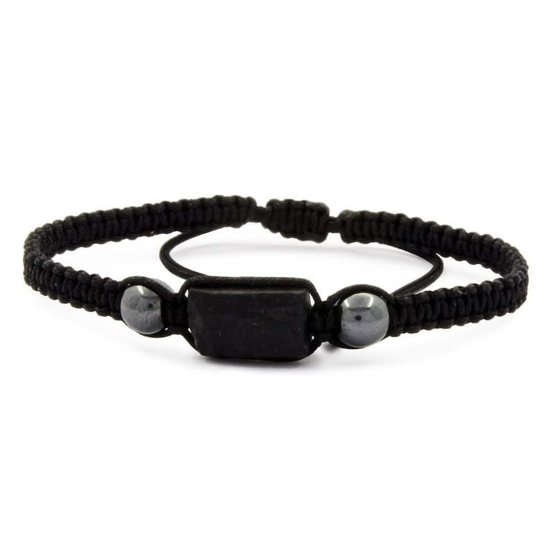 May include: Black macrame bracelet featuring a rectangular black stone center and two gray spherical beads. The adjustable bracelet is made of woven black cord. A simple, minimalist design.