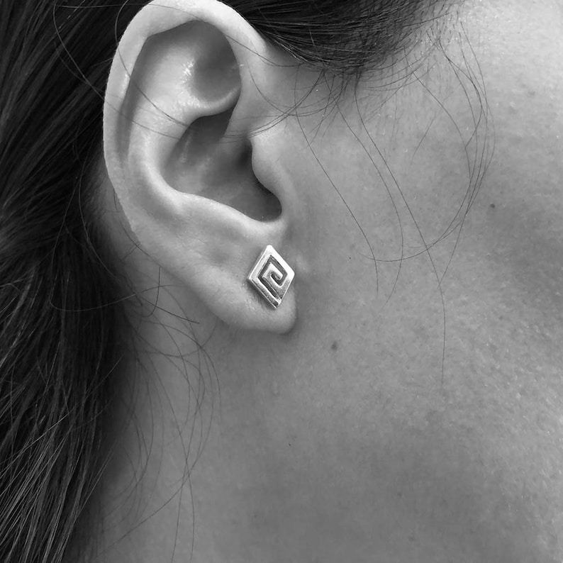 May include: A close-up of a person's ear with a small silver earring featuring a geometric spiral design.