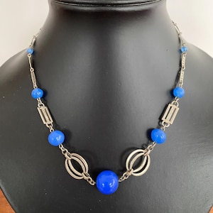 Puede incluir: Un collar de cadena de plata con cuentas de vidrio azul y detalles geométricos plateados.