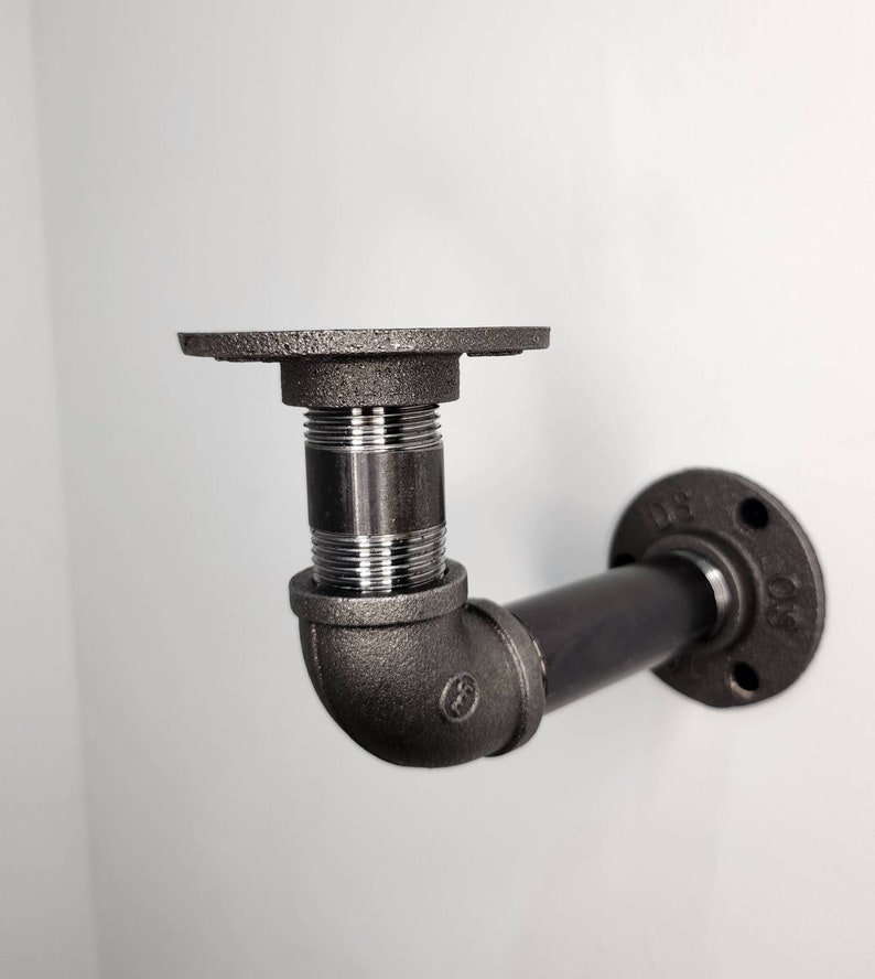 Puede incluir: Soporte de estante de tuber&iacute;a de metal negro con una brida en un extremo y un codo de 90 grados en el otro extremo. La tuber&iacute;a est&aacute; roscada y tiene un accesorio de color plateado.