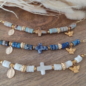 May include: Three bracelets with gold crosses and angel charms. Each bracelet features different colored stones: blue, white, and brown.