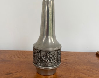 May include: A silver pewter vase with an embossed design of people in a boat. The vase has a narrow neck and a wide base.