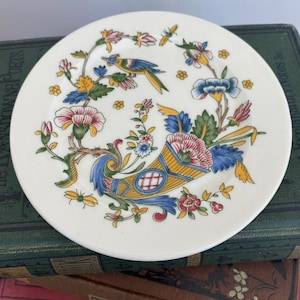 Puede incluir: Un plato de cerámica blanco con un diseño floral que presenta un pájaro, flores y una cornucopia. El diseño está en tonos de azul, amarillo, rojo y verde.