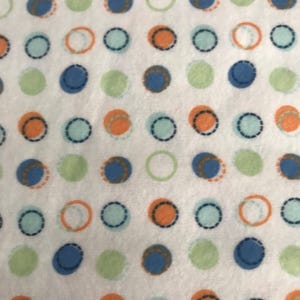 May include: White fabric featuring a repeating pattern of colourful polka dots. The dots are in shades of blue, orange, green, and light blue, with some outlined in a contrasting colour. The design is simple and playful.