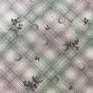 Puede incluir: Una tela blanca con un patrón de cuadros verdes y morados. La tela tiene una textura sutil y está decorada con pequeños diseños florales.