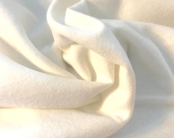 Op de afbeelding: Close-up van een witte stof met een zacht, getextureerd oppervlak. De stof is gevouwen en gedrapeerd, waardoor de gladde en gelijkmatige textuur zichtbaar is.