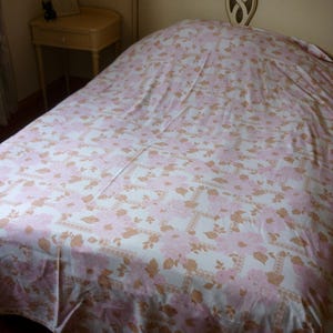 May include: A white bed with a pink and brown floral patterned bedspread. The bed has a white headboard with a decorative design.