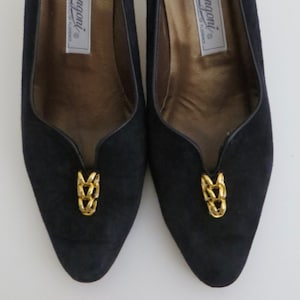 May include: Pair of black suede pumps with gold chain accents. The shoes have a pointed toe and a low heel. The brand name "Rangoni" is printed on the insole.