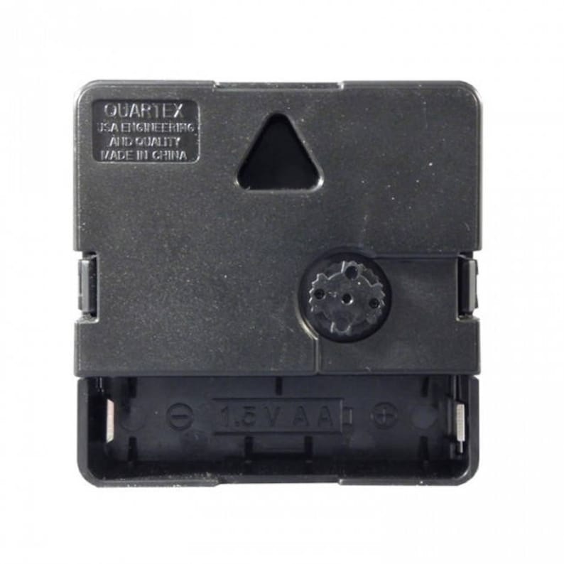 May include: A black clock movement with a 1.5V AA battery compartment. The movement has a small triangle cutout and the text "QUARTEX USA ENGINEERING AND QUALITY MADE IN CHINA".