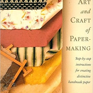 May include: The cover of "The Art and Craft of Paper-Making" book. The image shows a stack of colorful handmade papers with various textures and patterns. The book's title and author, Sophie Dawson, are visible.