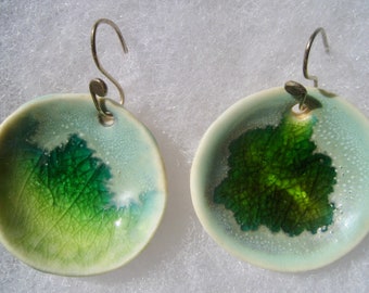 May include: A pair of ceramic earrings with a green leaf design on a white and blue background. The earrings have silver hooks.