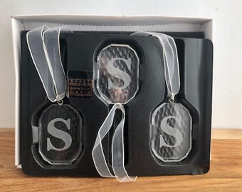 May include: Three clear crystal ornaments with the letter "S" etched on them, each hanging from a white ribbon. The ornaments are displayed in a black box with a Fifth Avenue Crystal label.