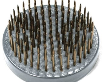 May include: A round, gray floral foam base with gold-colored metal pins. The pins are arranged in a circular pattern and are evenly spaced.
