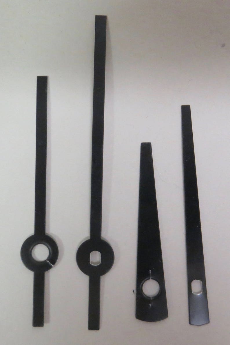 May include: Four black clock hands of different sizes. The hands are made of metal and have a hole in the center for attaching to a clock mechanism.